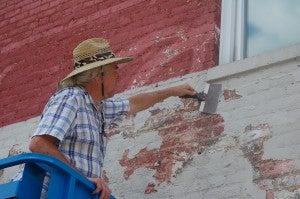 JORDAN MILES | HERALD Ron Sacks scrapes a ghost mural at the corner of West Third and North streets in preparation for restoration of a Coca-Cola mural.