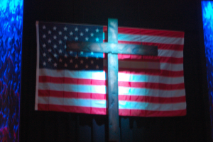 TITUS MOHLER | HERALD A cross stands in front of the American flag during New Life Church’s Valor Day Program on Sunday. 